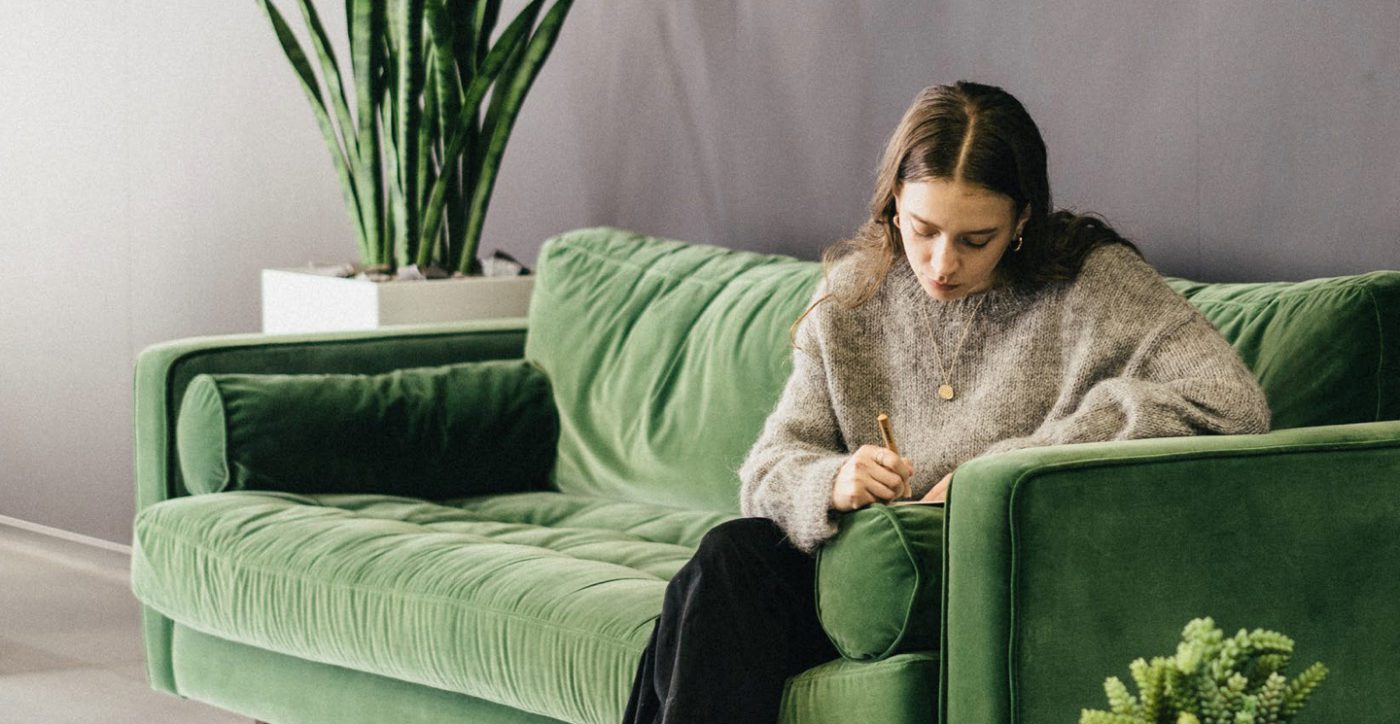 woman writing while sitting on green sofa