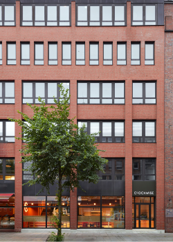 A red brick office building with large windows, a tree in front, and a sign reading 